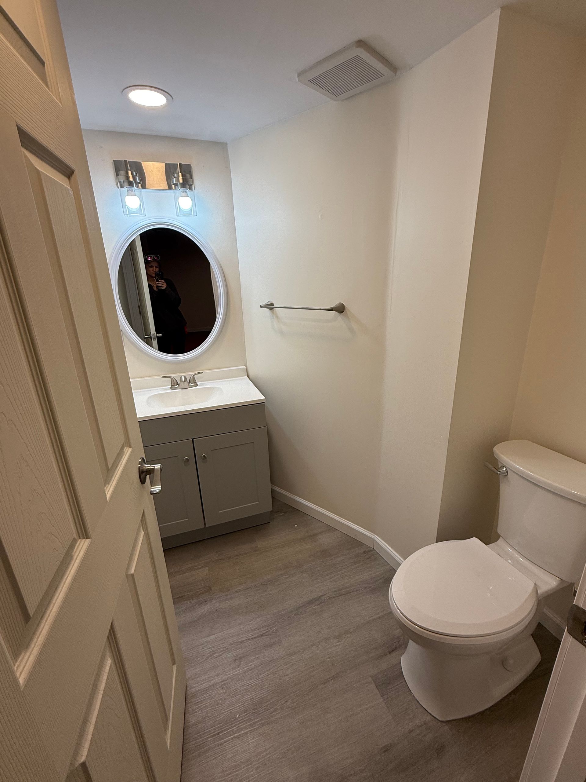 Small bathroom with a toilet, vanity with mirror, and towel rack. Door on the left.