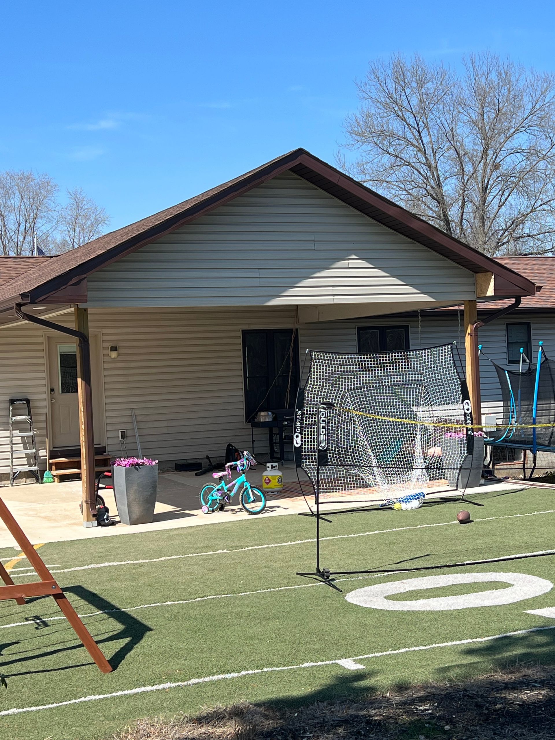 Backyard with covered porch, artificial turf football field, children's toys, sunny day.