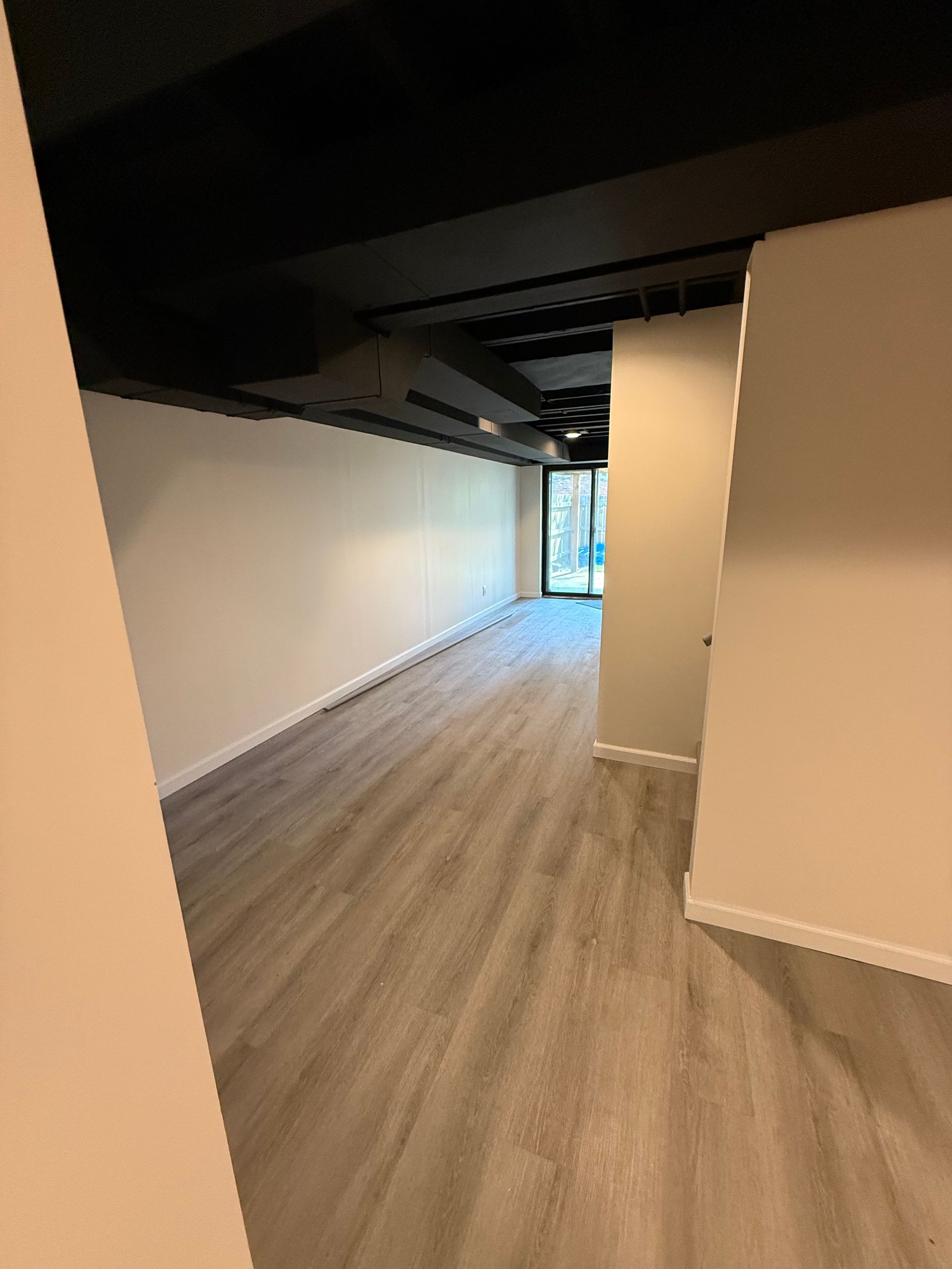 Long, empty room with light gray flooring, white walls, and a black ceiling.