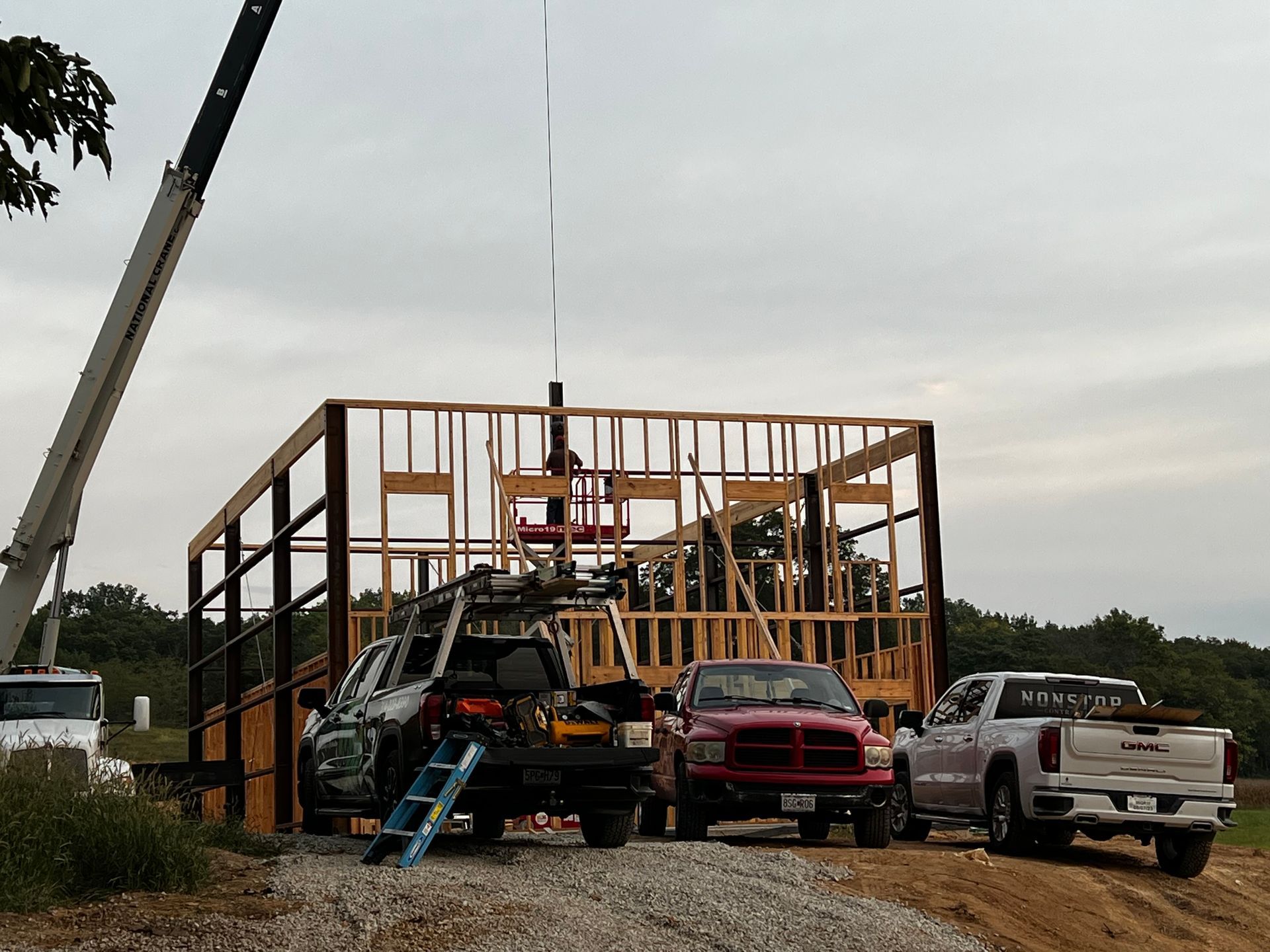 Construction site with wooden frame and trucks; crane lifting.