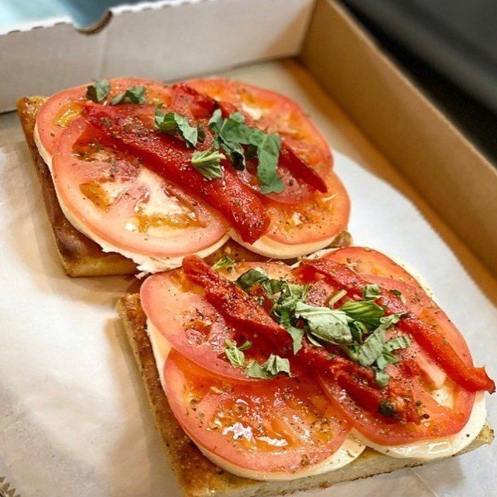 Two sandwiches with tomatoes and peppers in a box