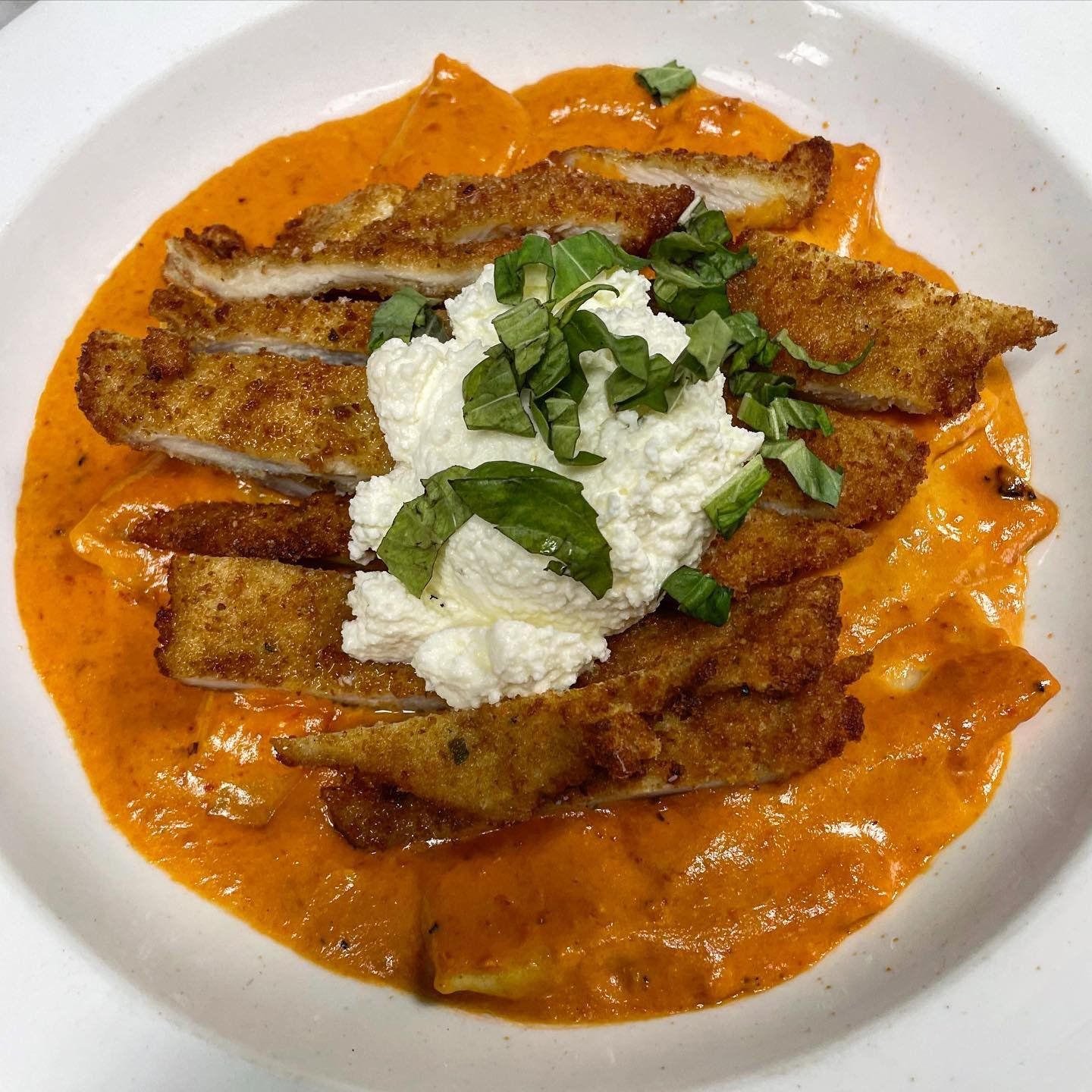 A close up of a plate of food with chicken and sauce on a table.