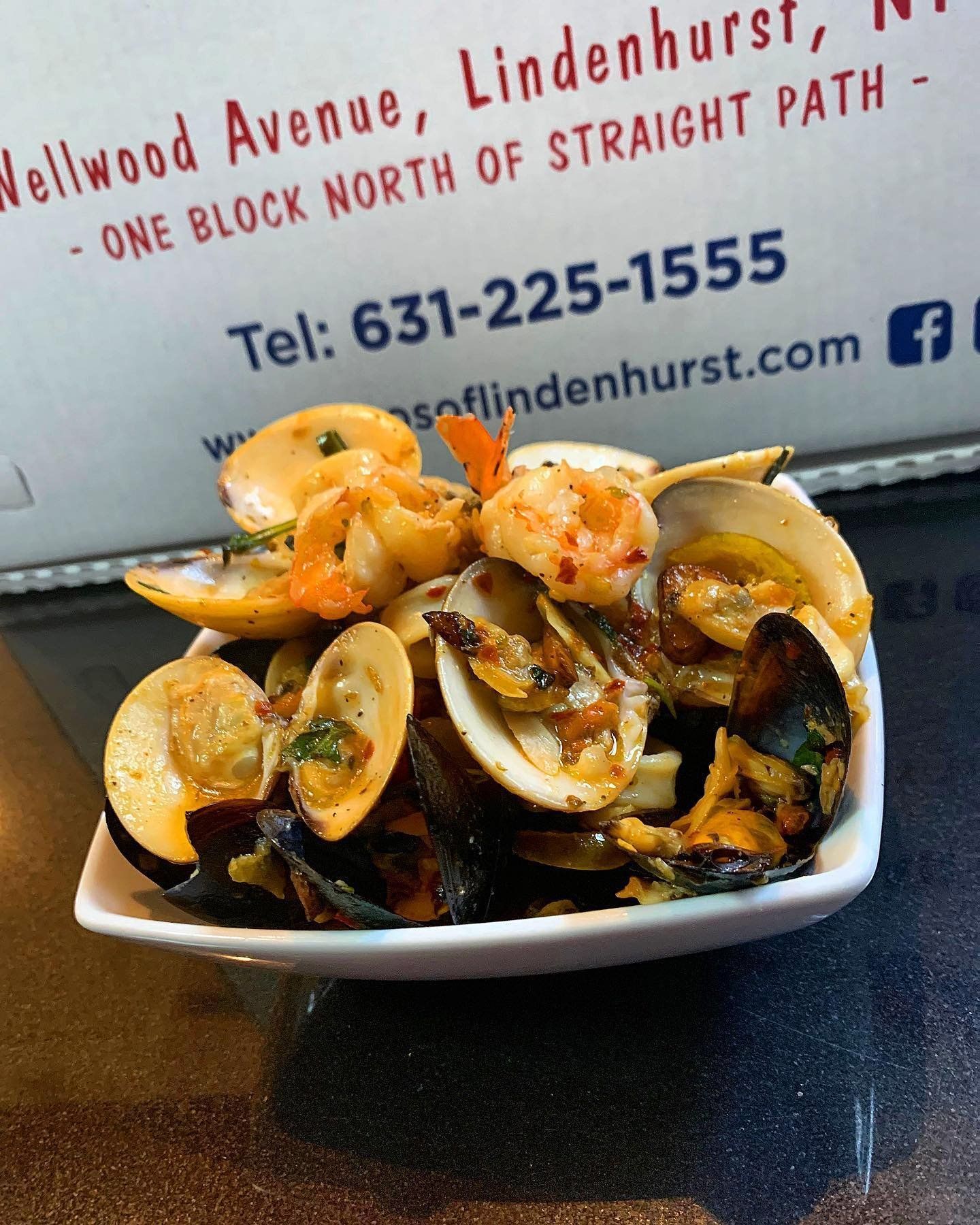 A plate of seafood sits in front of a sign that says wellwood avenue lindenhurst one block north of straight path