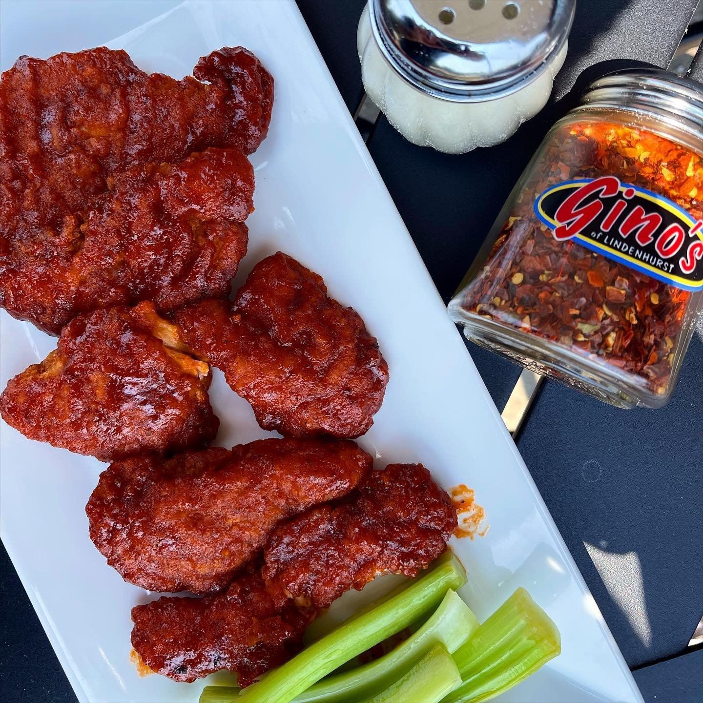 A white plate topped with chicken wings and celery next to a jar of gino 's seasoning