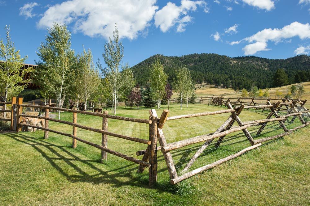 A wooden fence surrounds a grassy field with mountains in the background.