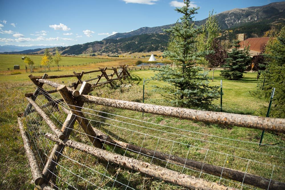 A wooden fence with barbed wire surrounding a field with mountains in the background.