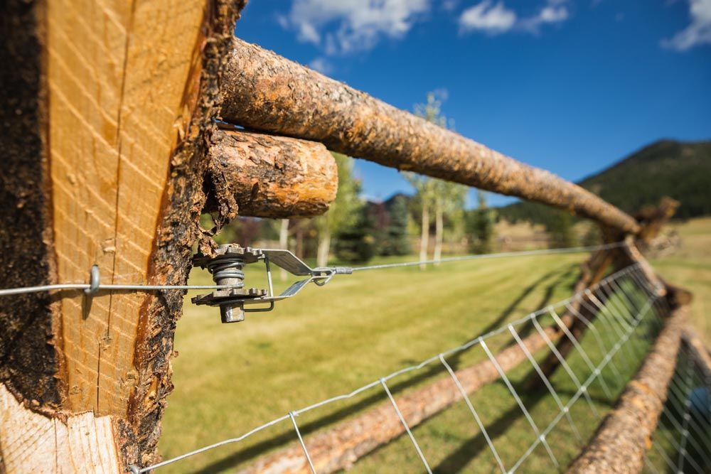 A close up of a wooden fence with a wire fence in a field.