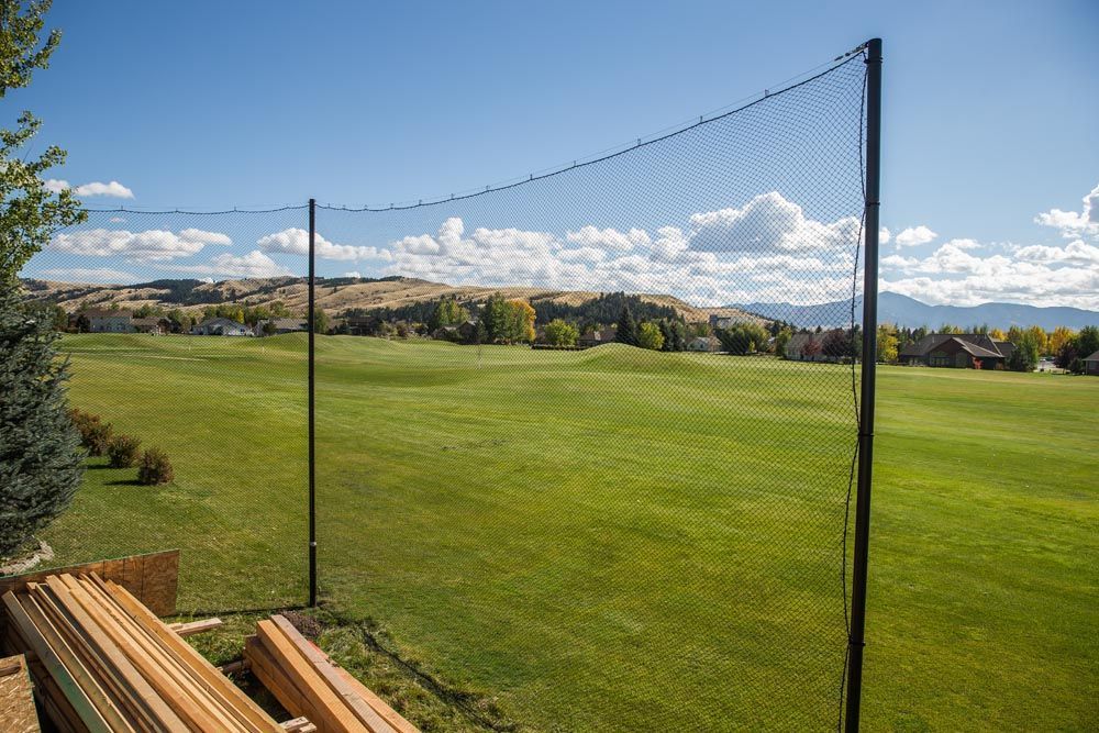 A golf course with a fence in the foreground and a stack of wood in the background.