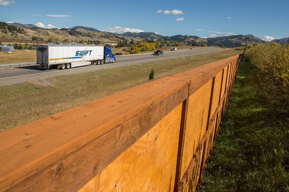 A truck is driving down a highway next to a wooden fence.