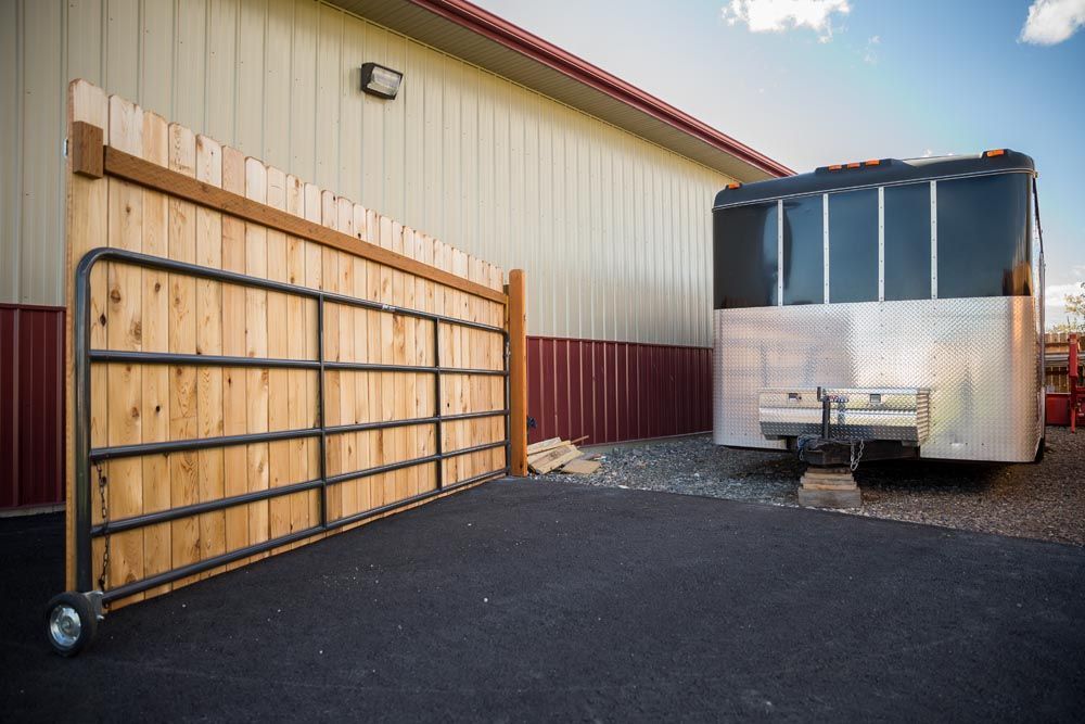 A trailer is parked in front of a building next to a wooden gate.