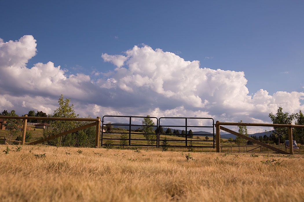 There is a fence in the middle of a field with a cloudy sky in the background.