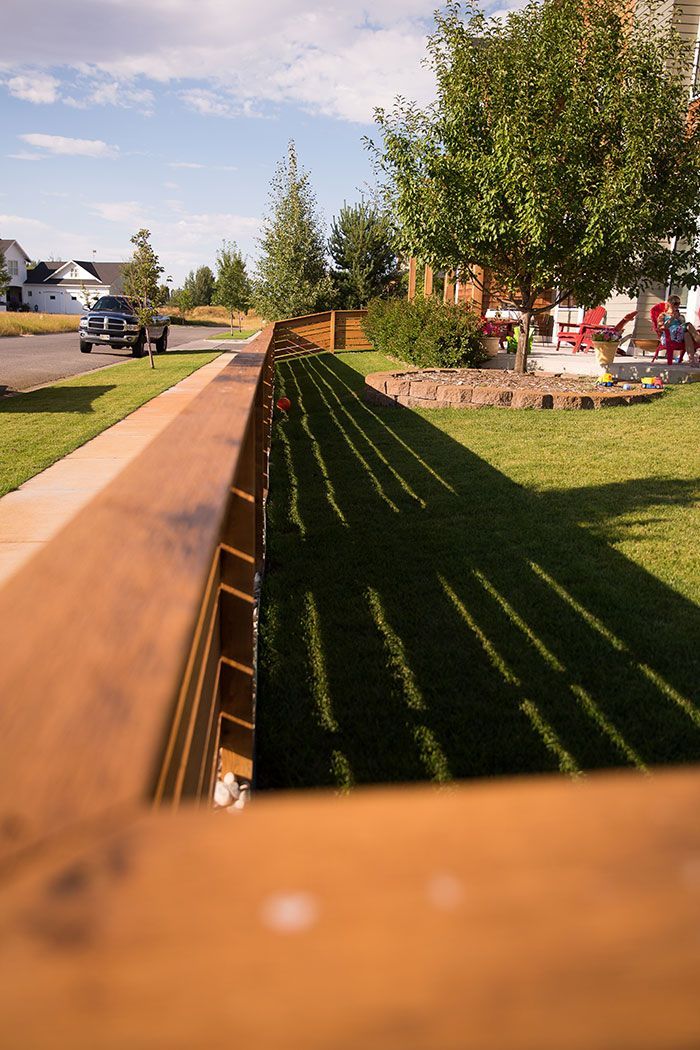 A wooden fence surrounds a lush green lawn in a residential neighborhood.