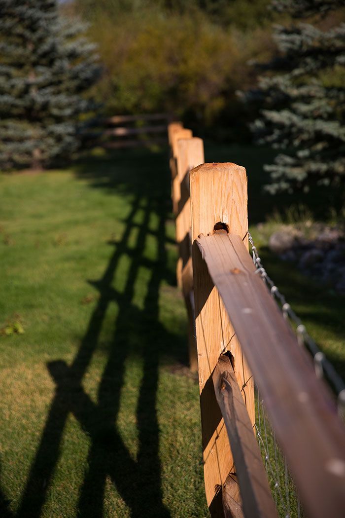 A close up of a wooden fence with a shadow on the grass.