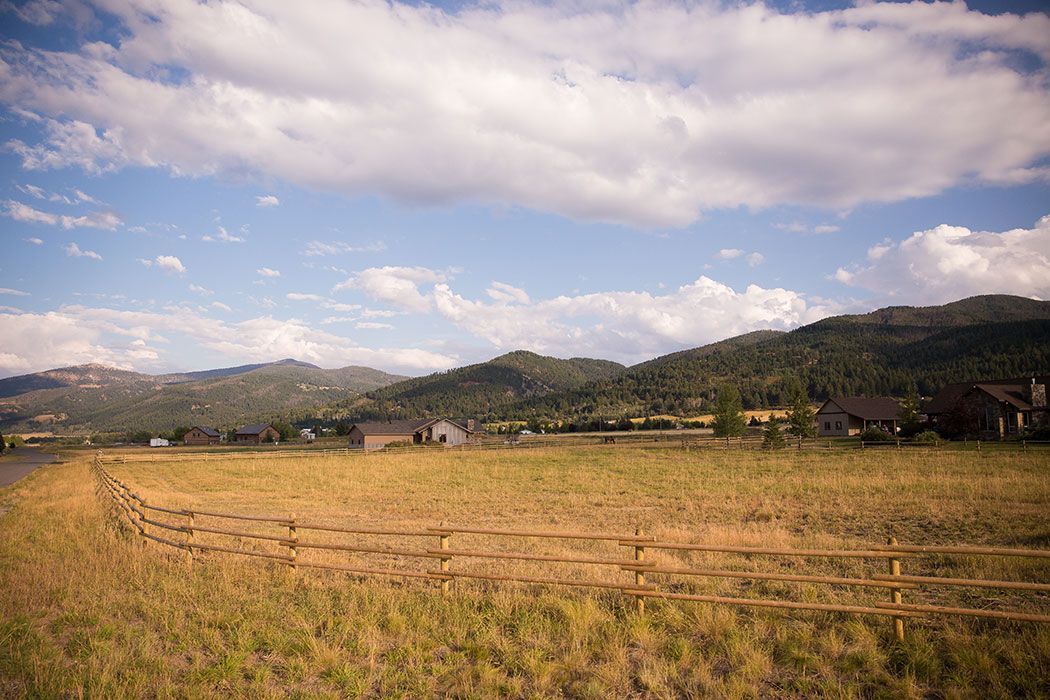 A wooden fence surrounds a grassy field with mountains in the background.