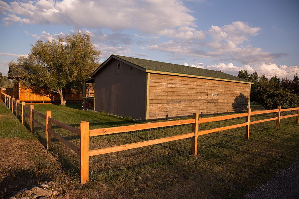 A wooden fence surrounds a shed in a grassy field.