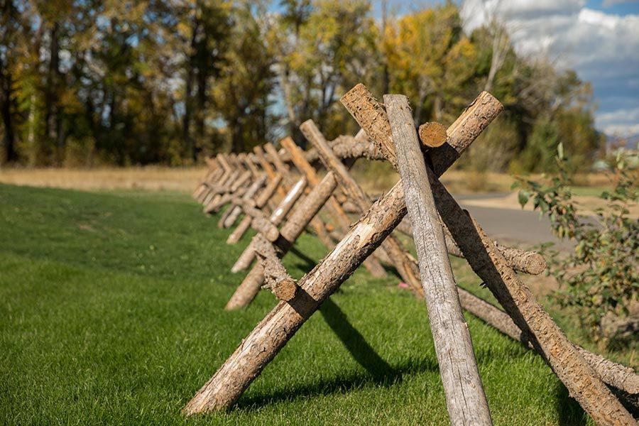 A wooden fence made of logs is sitting on top of a lush green field.