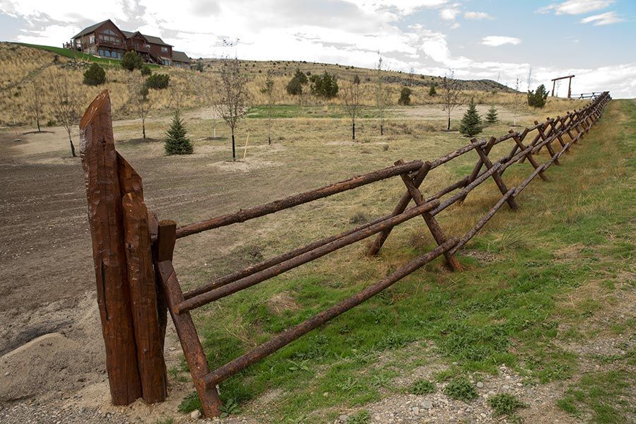 A wooden fence surrounds a grassy field with a house in the background.
