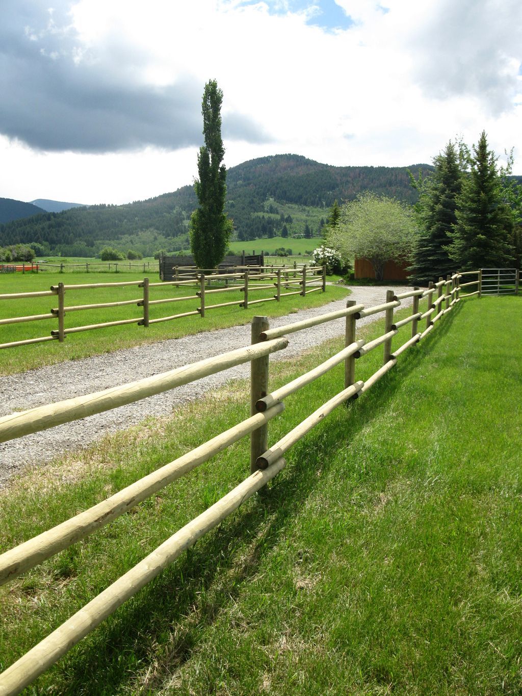 A wooden fence surrounds a grassy field with mountains in the background.