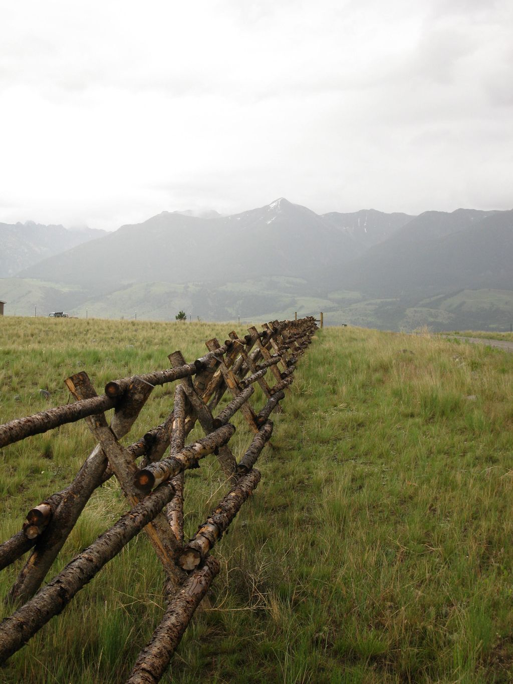 A wooden fence surrounds a grassy field with mountains in the background.