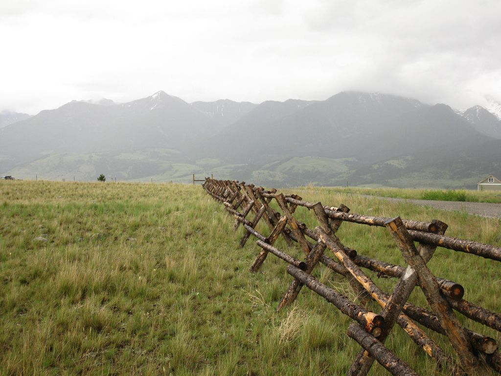 A wooden fence surrounds a grassy field with mountains in the background.