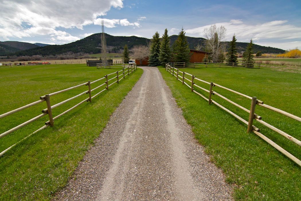 A dirt road with a wooden fence going through a grassy field.