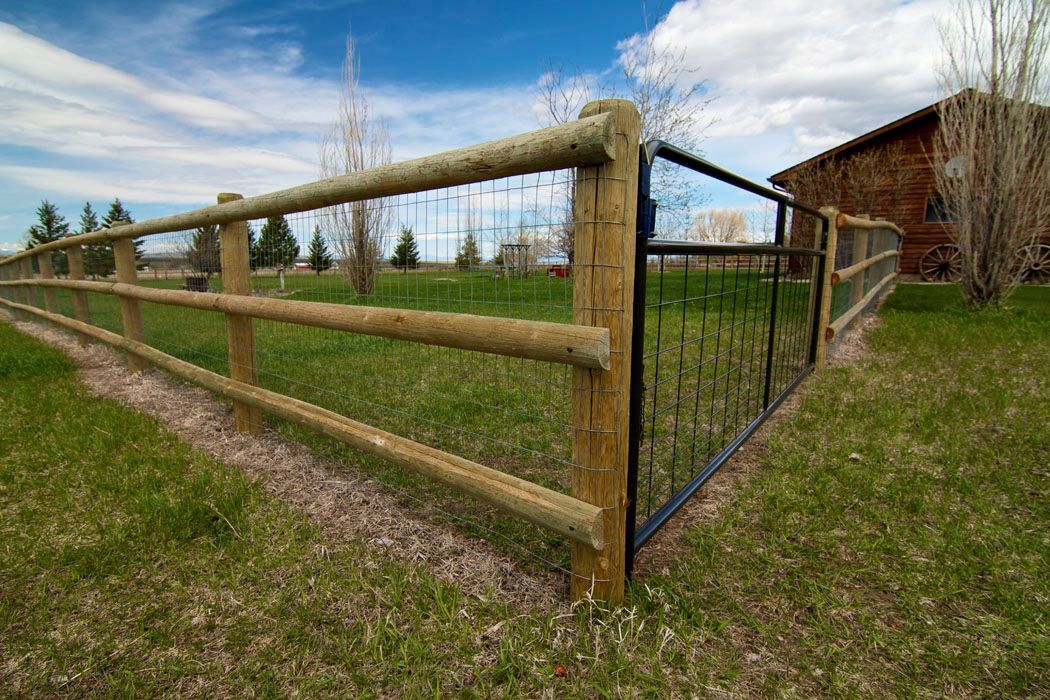 A wooden fence with a metal gate is surrounding a grassy field.