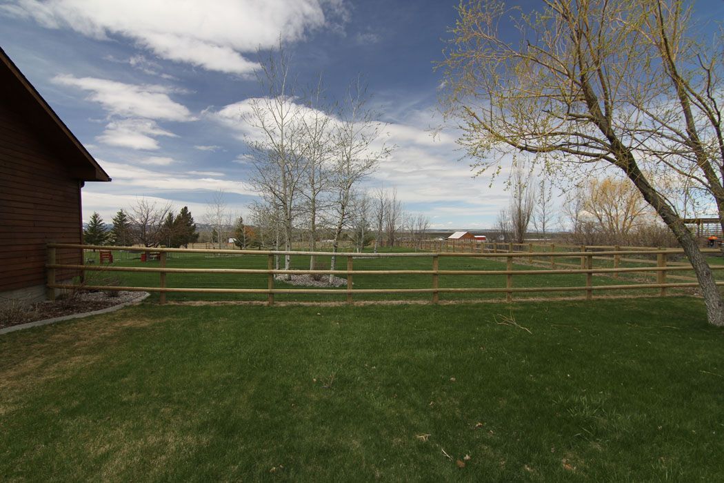 A wooden fence surrounds a grassy field in front of a house.