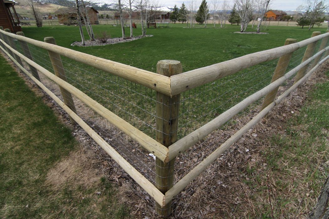 A wooden fence surrounds a lush green field.
