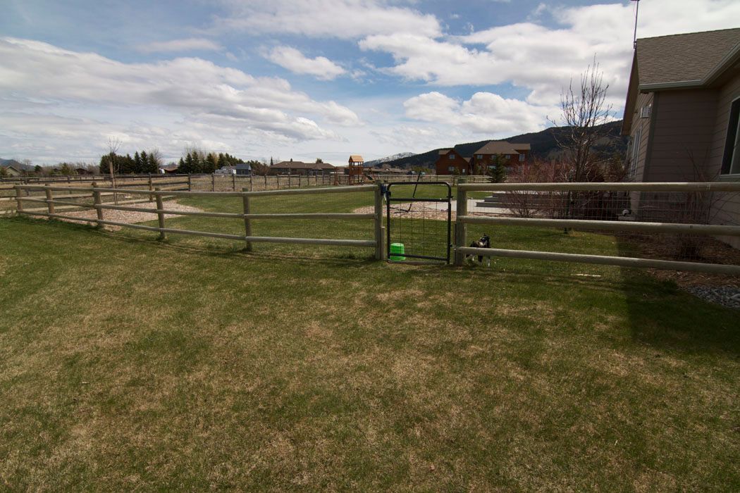 A fence surrounds a grassy field with a house in the background.