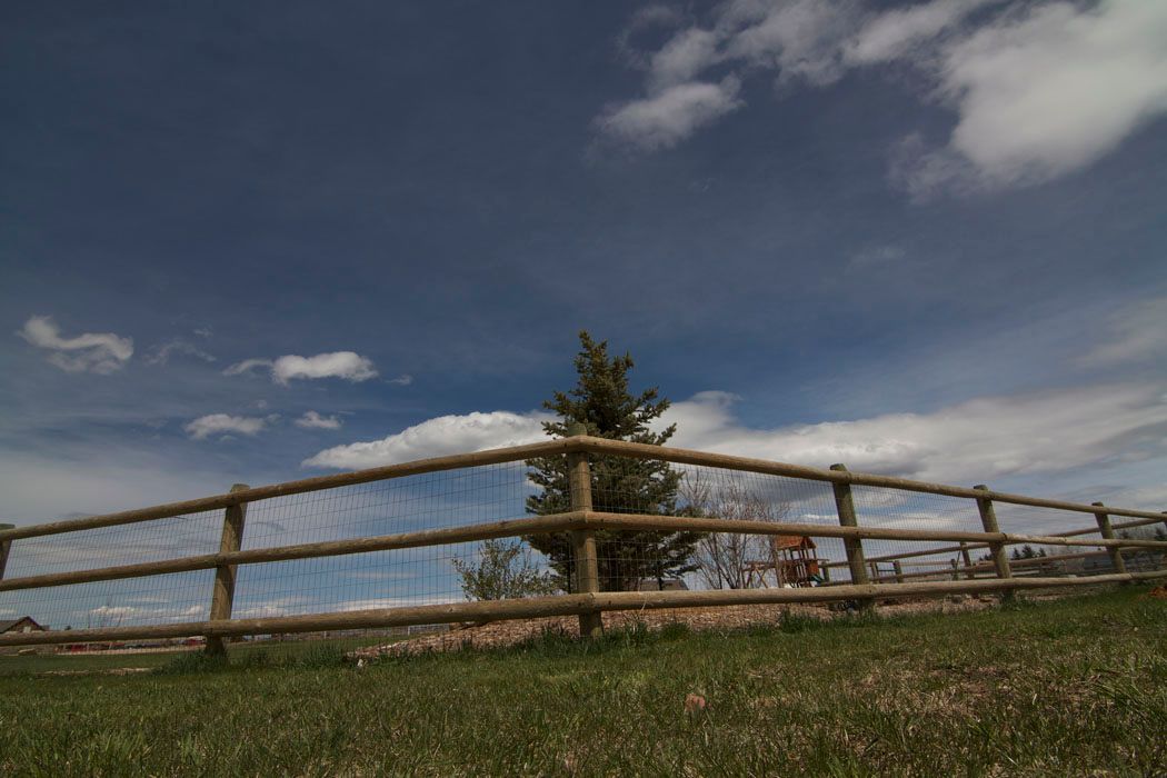 A wooden fence surrounds a grassy field with a tree in the background.