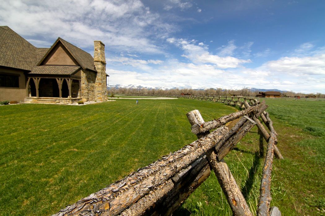 A wooden fence surrounds a lush green field in front of a house.