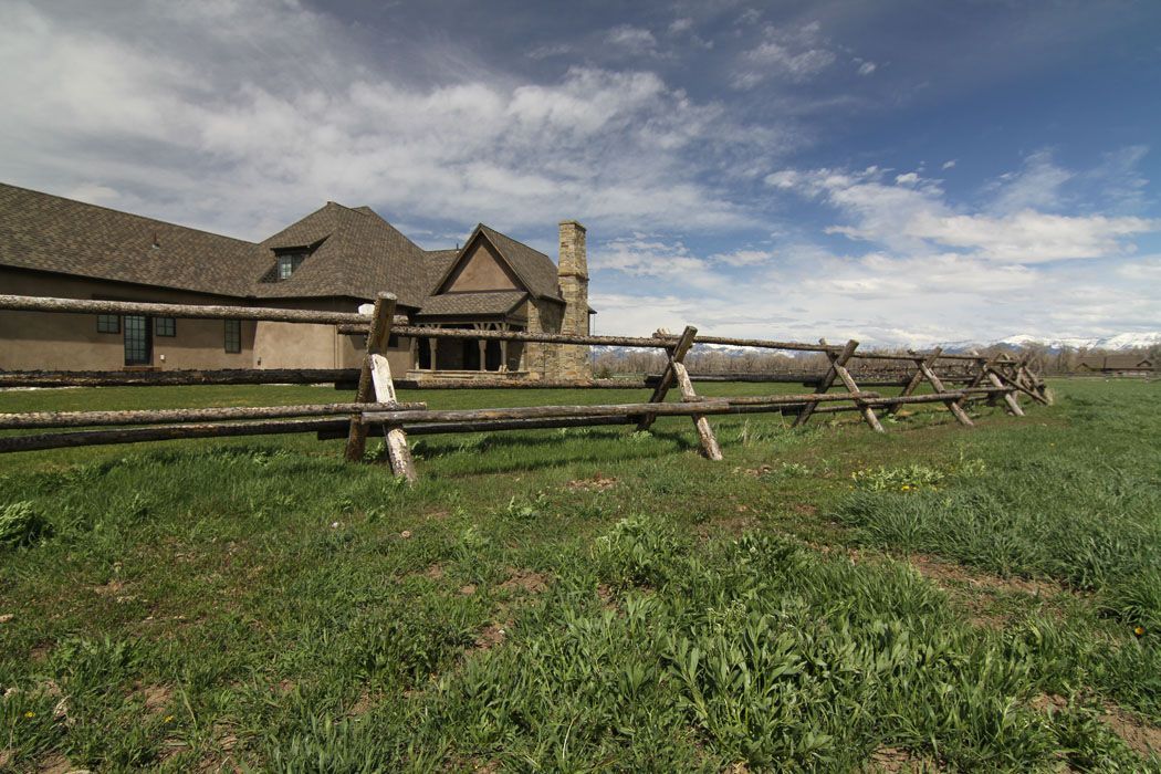 A large house is behind a wooden fence in a grassy field.