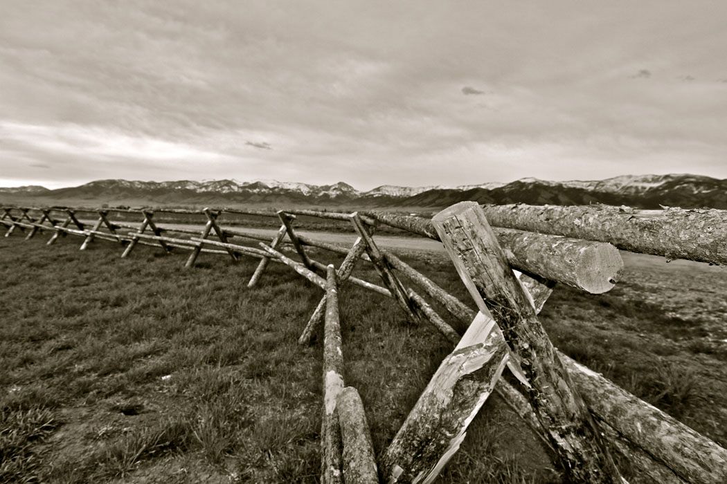A black and white photo of a wooden fence in a field.