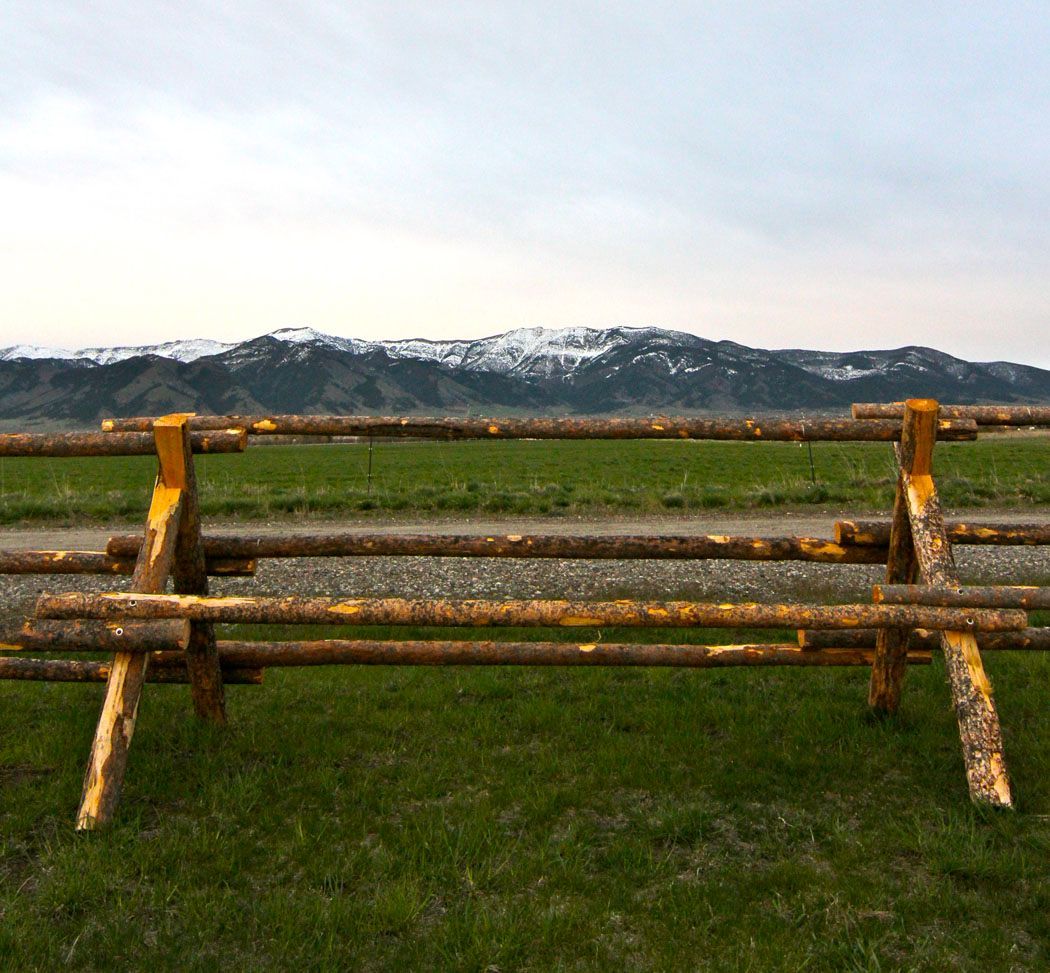A wooden bench is sitting in the middle of a grassy field with mountains in the background.
