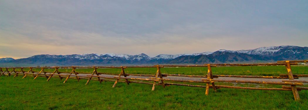 A wooden fence surrounds a grassy field with mountains in the background.