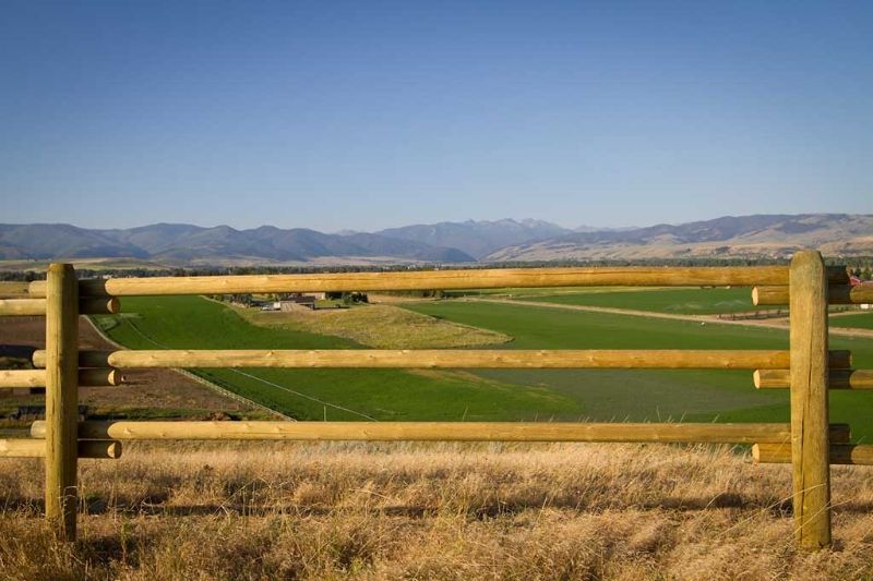 A wooden fence surrounds a field with mountains in the background.