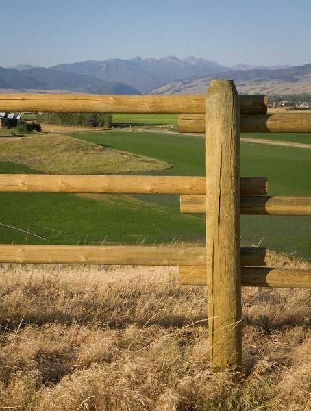 A wooden fence surrounds a field with mountains in the background.