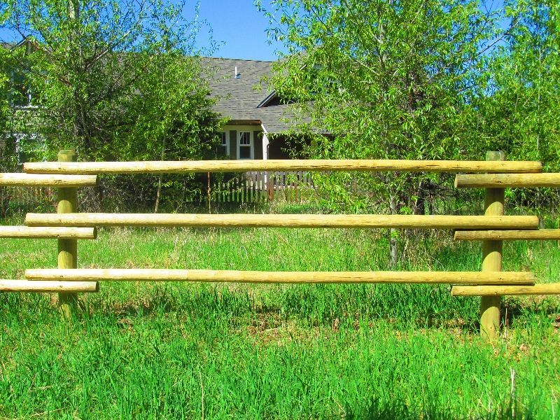 A wooden fence in a grassy field with a house in the background.