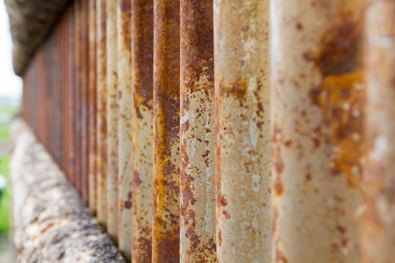A close up of a rusty metal fence with a blurred background.