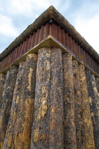 The corner of a wooden building with a thatched roof.