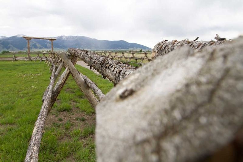 A wooden fence surrounds a grassy field with mountains in the background.