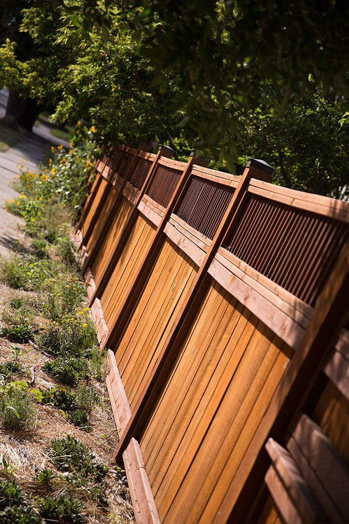 A wooden fence is surrounded by trees and grass on the side of a road.