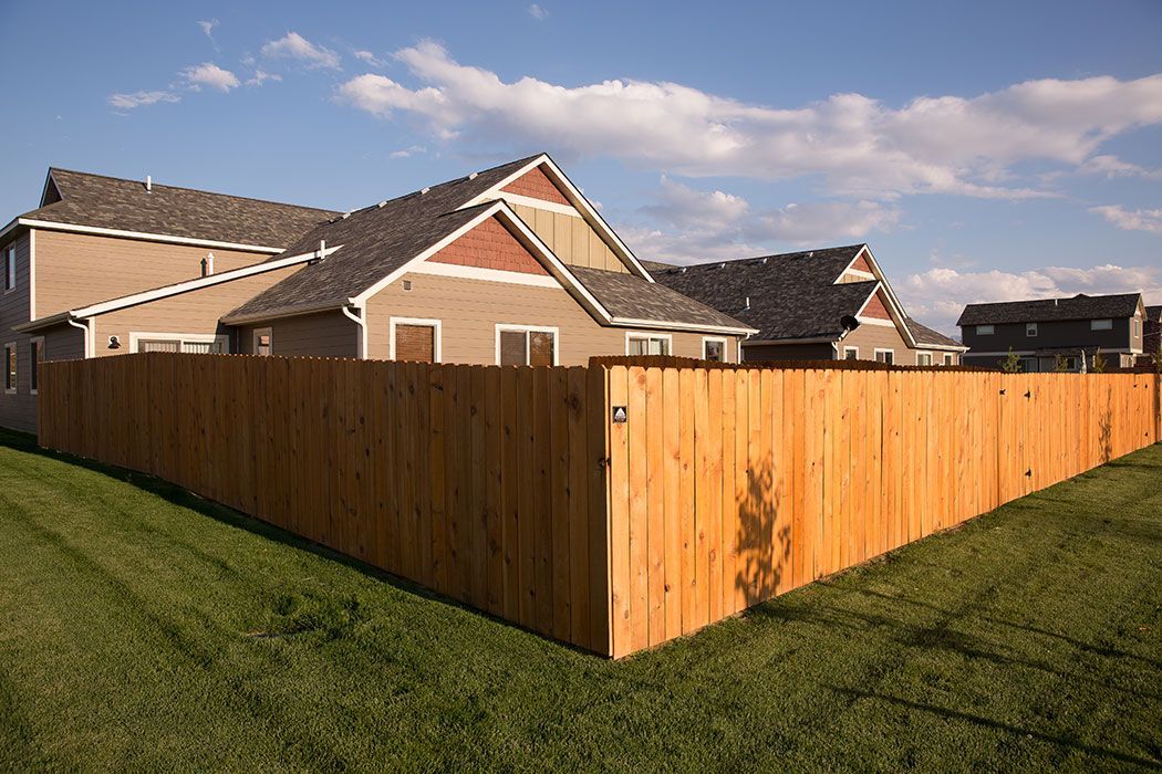 A wooden fence surrounds a lush green yard in front of a house.