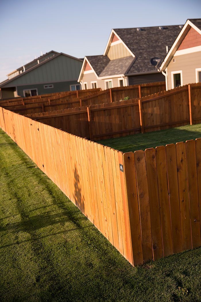 A wooden fence surrounds a lush green yard in front of a row of houses.