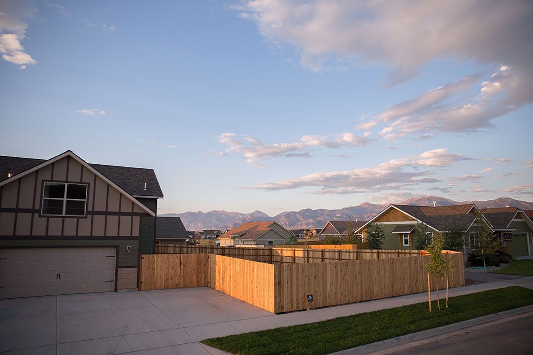 A wooden fence surrounds a house in a residential area with mountains in the background.