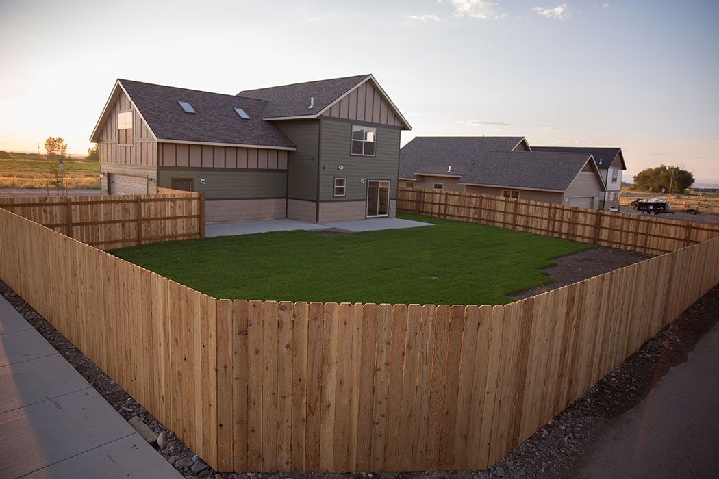 A wooden fence surrounds a lush green yard in front of a house.
