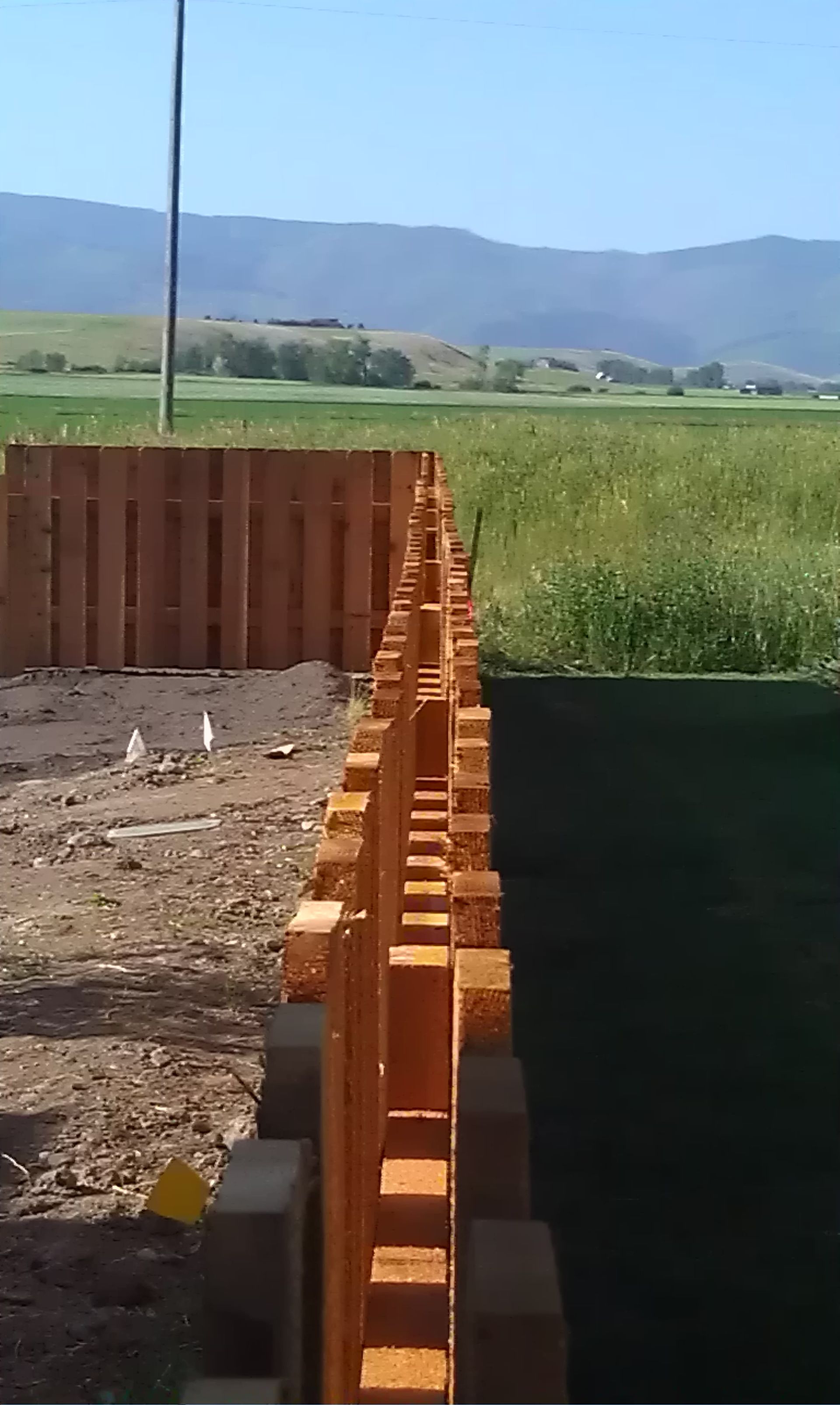 A wooden fence is being built in a field with mountains in the background.
