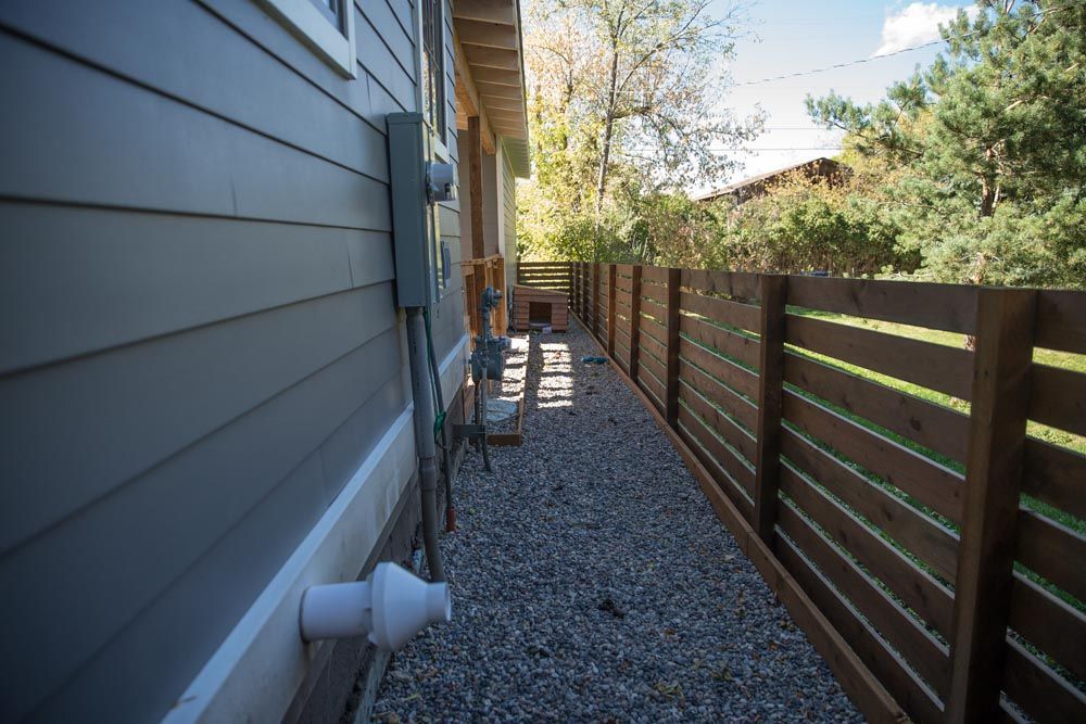 A house with a wooden fence and gravel in front of it.