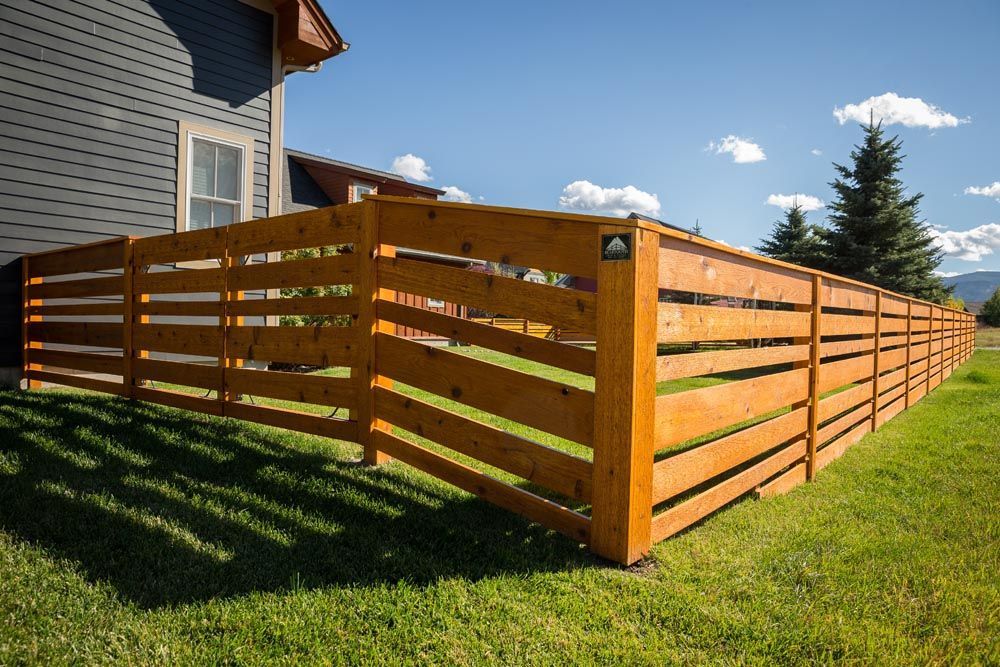 A wooden fence is in the grass in front of a house.