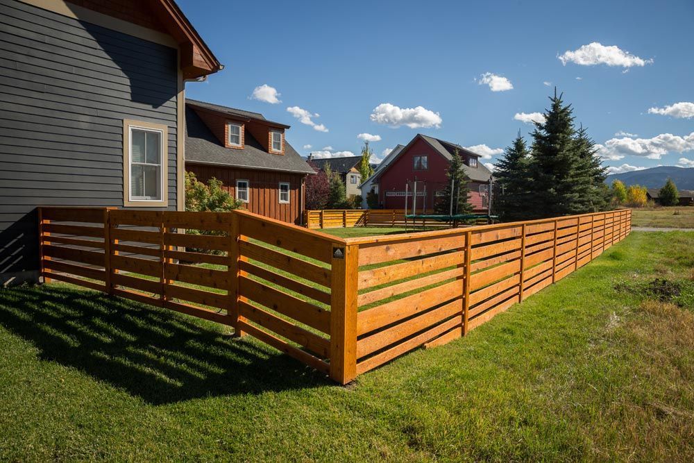A wooden fence surrounds a lush green yard in front of a house.